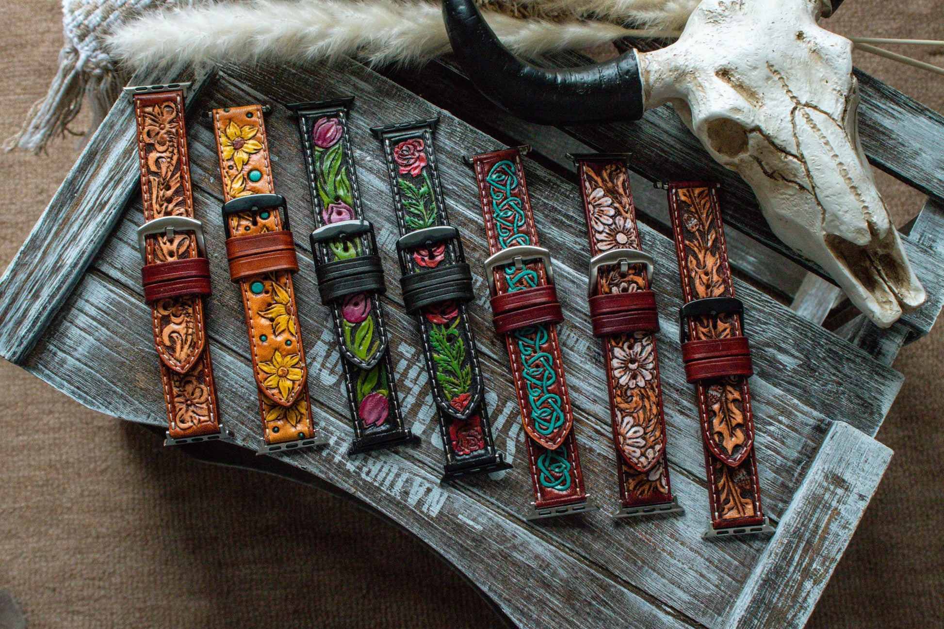 Collection of handcrafted tooled leather Apple Watch bands featuring boho sunflower, turquoise Celtic, oak leaf, red rose, tulip, and western floral designs