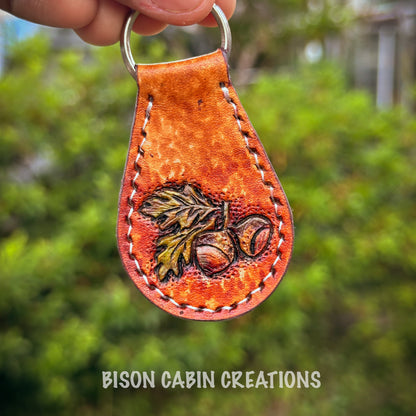 Hand holding a leather keychain with oak fruit design 