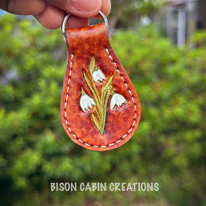 Hand-made, tooled leather keychain featuring Lilly flowers, rustic hand-painted details with medium brown leather, nature-inspired key fob.