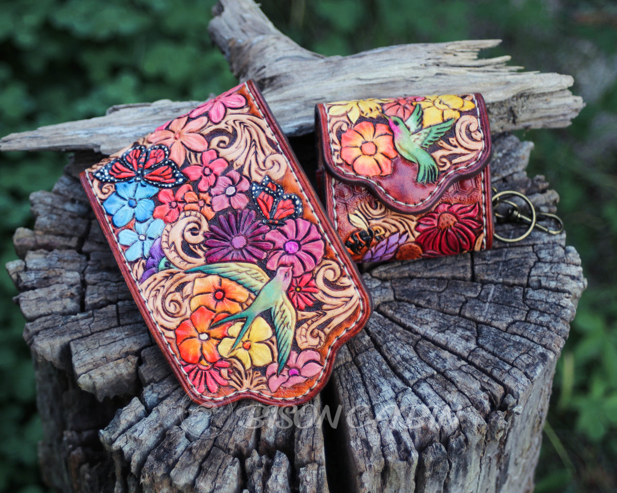 Handmade leather AirPods pouch featuring intricate floral tooling and a hummingbird and song birds .