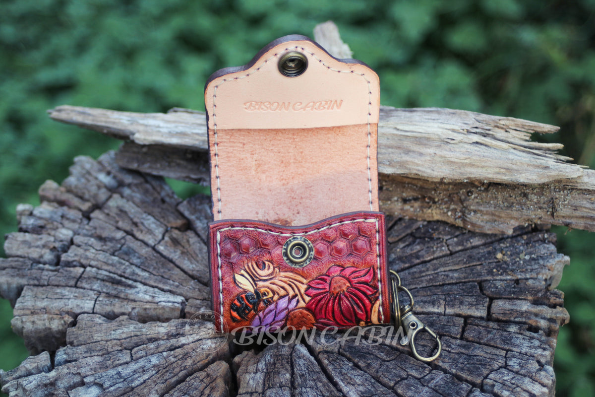 Artistic tooled leather AirPods holder decorated with vibrant blossoms, Bee ,swirling patterns, and bird details.