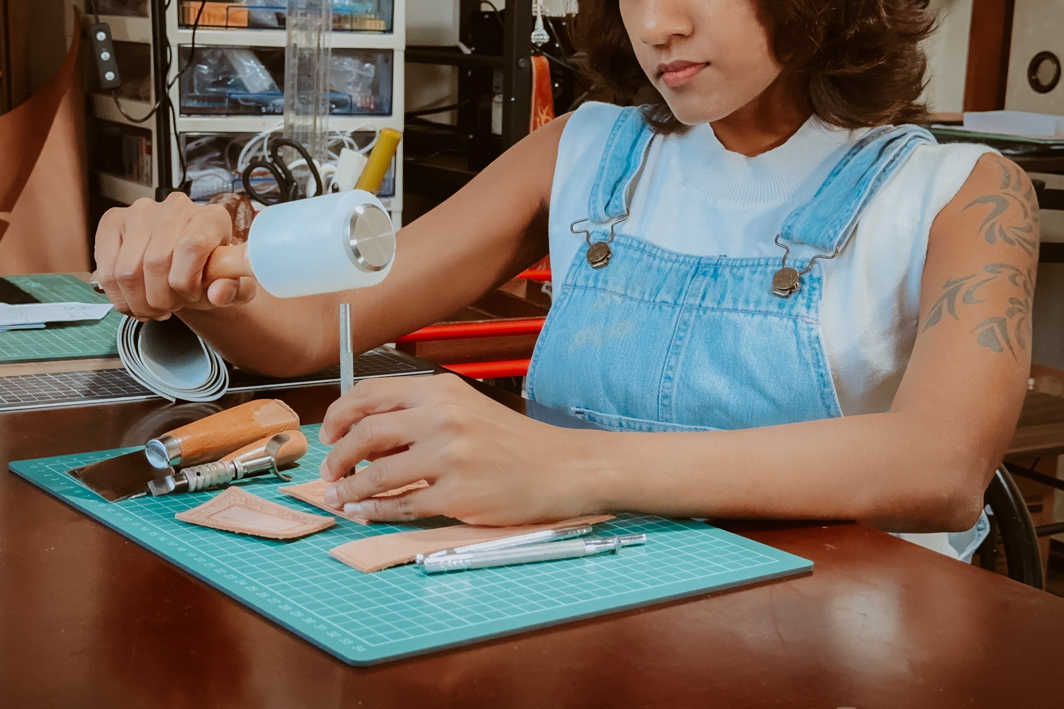 A leather craftsman is working on a craft project at a table with leather-stamped tools and materials.