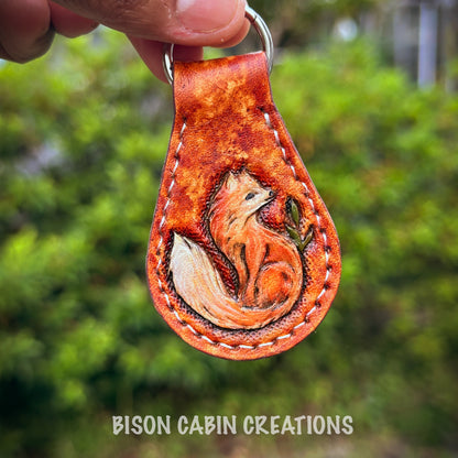 Hand-made, tooled leather keychain featuring red fox, rustic hand-painted details with medium brown leather, and nature-inspired key fob.