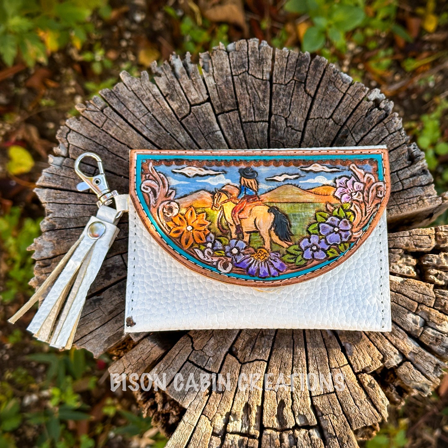 Premium handcrafted Tochigi leather wallet with vibrant western artwork, floral carving, and white pebble leather base, photographed on wood stump.
