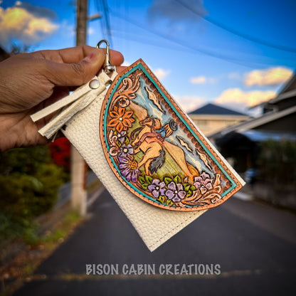 Detailed western leather wallet showing a cowgirl on horseback among flowers and landscape, accented with colorful tooling and attached white leather tassel.