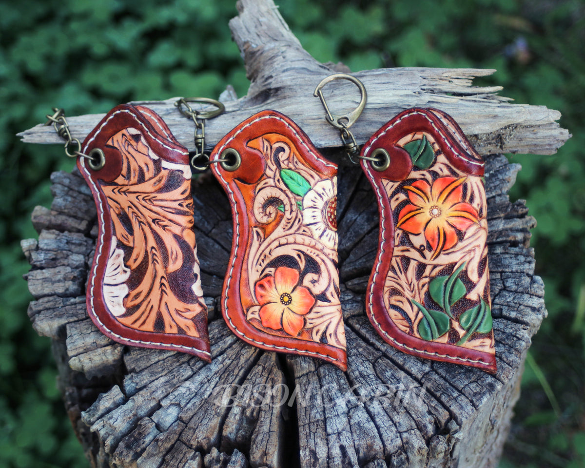 Hand-carved leather lighter case with an orange flower, green leaves, and decorative Western scroll patterns on genuine leather.