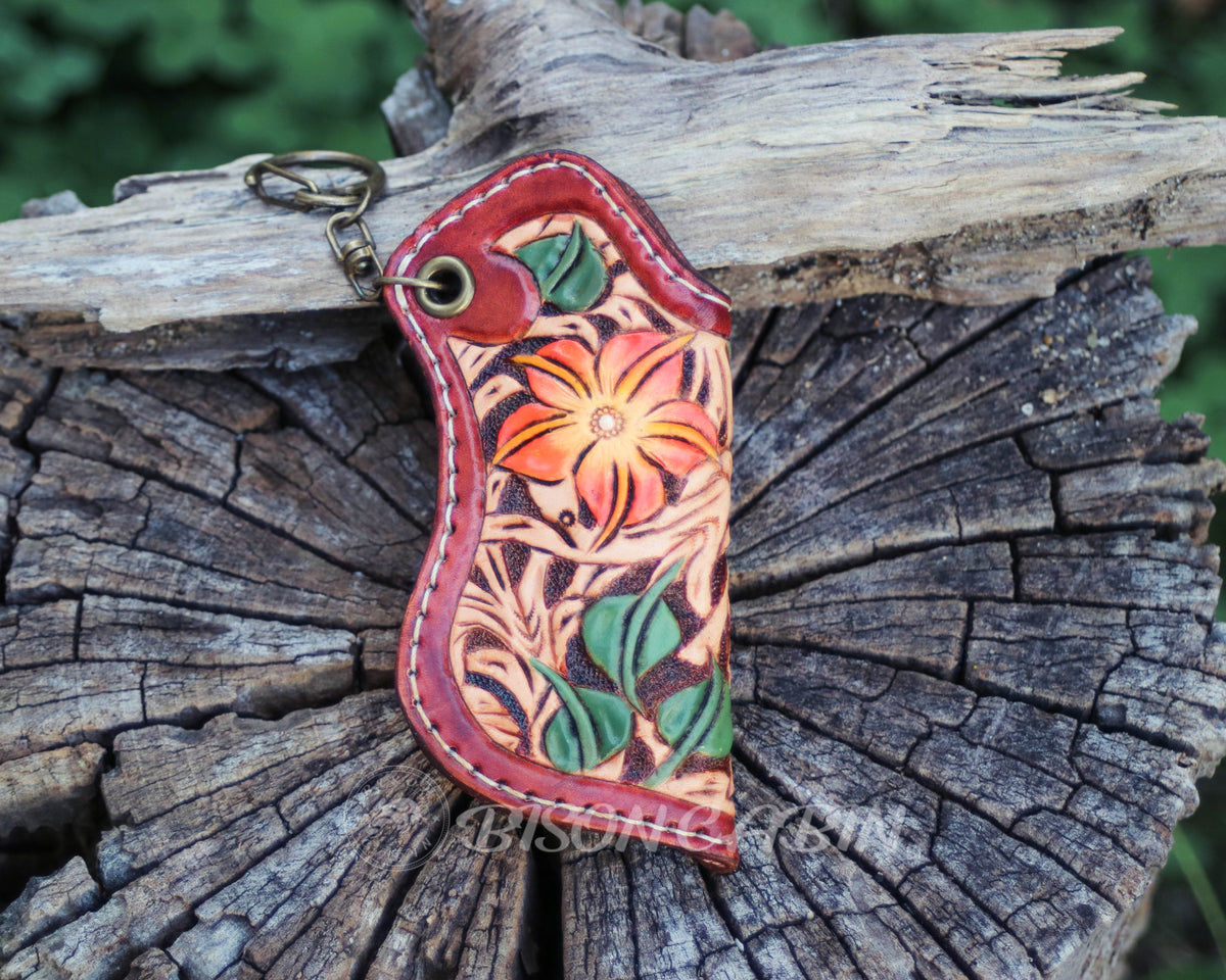 Hand-tooled Western leather lighter holder with a vibrant orange floral design, green leaf details, burgundy leather edges, and a decorative keychain attachment.