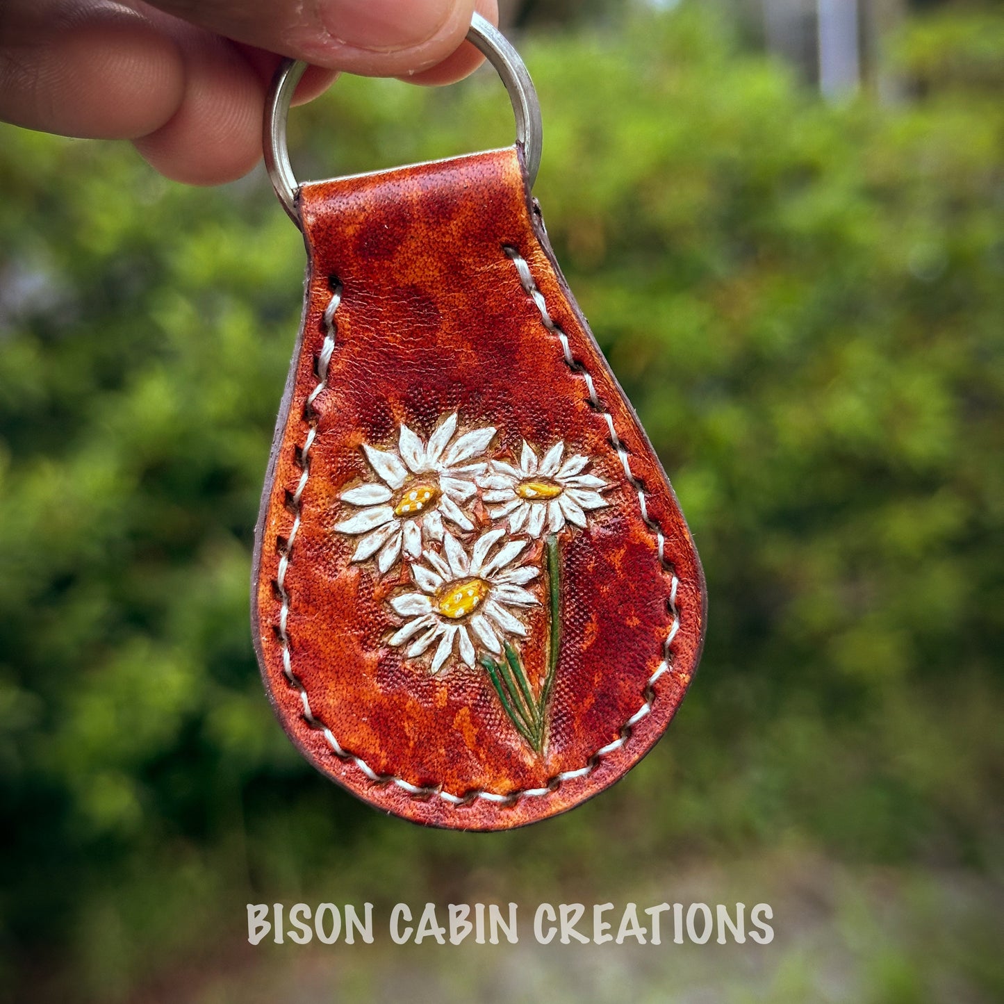 Hand-made, tooled leather keychain featuring Daisy’s flowers, rustic hand-painted details on brown leather, nature-inspired key fob.
