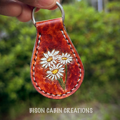 Hand-made, tooled leather keychain featuring Daisy’s flowers, rustic hand-painted details on brown leather, nature-inspired key fob.