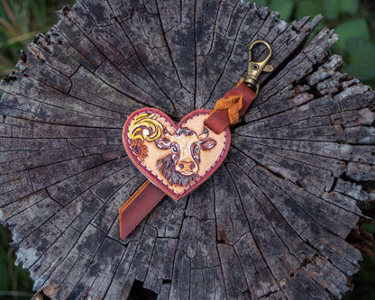 Handcrafted tooled leather heart charm featuring a detailed cow design, rustic Western style keychain with hand carved leather detailing and charm accessory finish