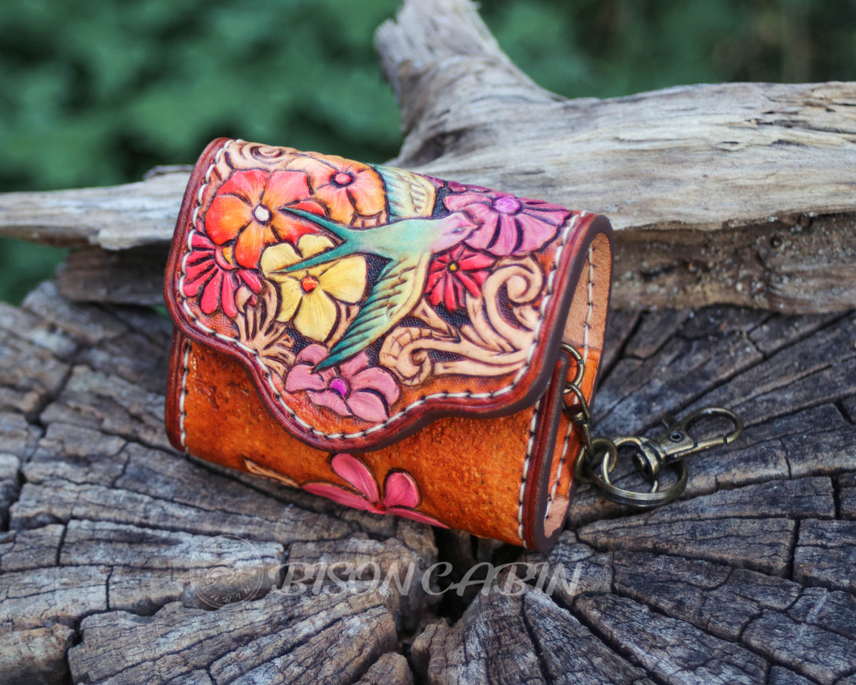 Artistic tooled leather AirPods holder decorated with vibrant blossoms, swirling patterns, and sparrow bird details.